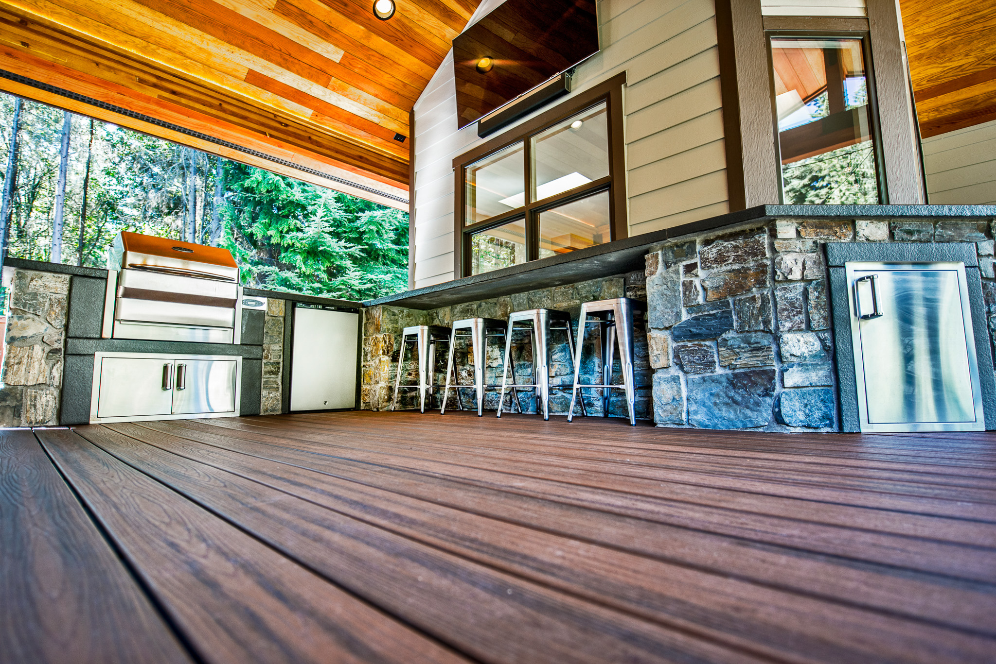 A large outdoor kitchen with natural stone on top of a wood deck