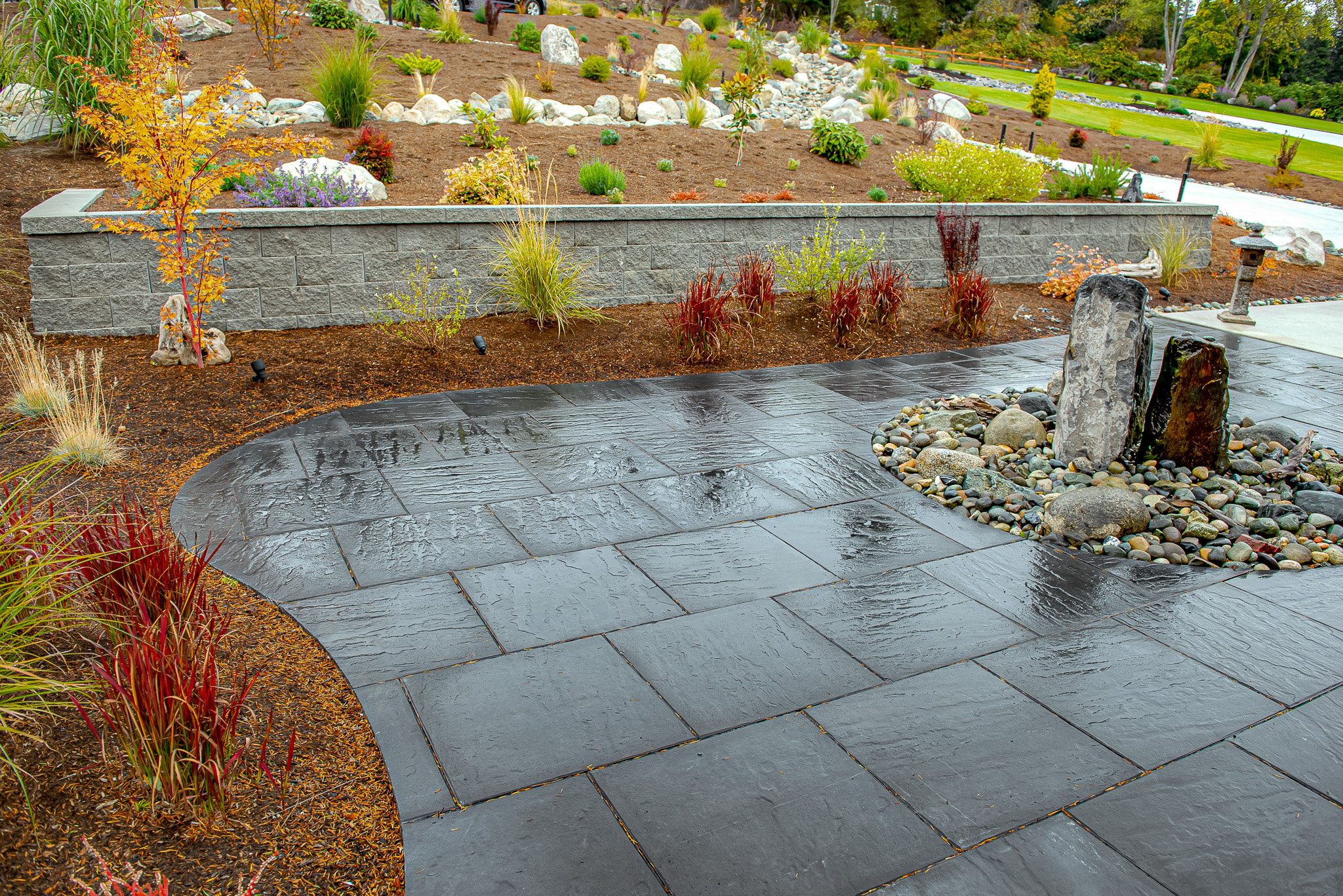 Architectural slab patio with water feature fronts a retaining wall