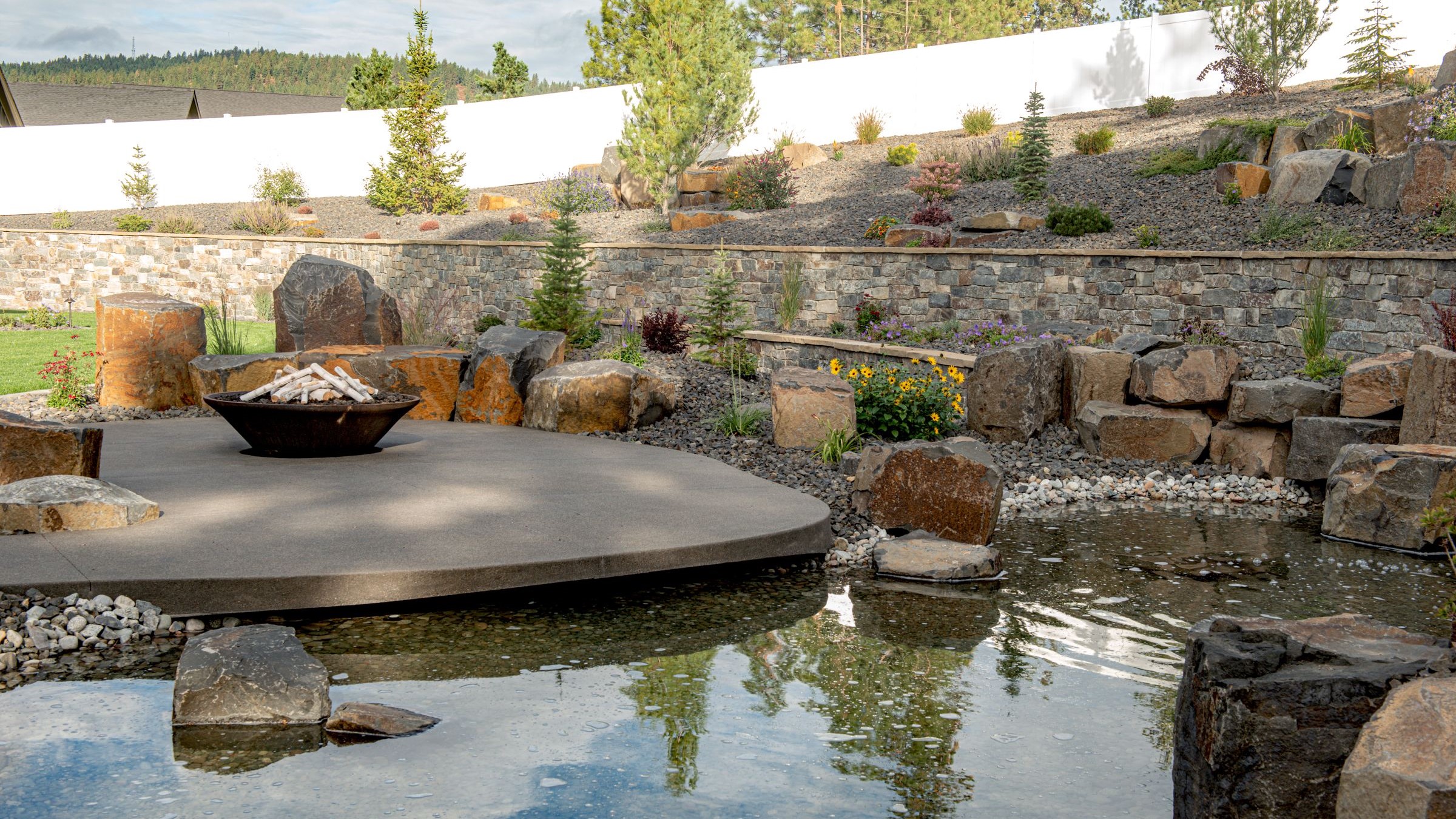 Modern circular patio surrounded by a water feature and natural stone retaining wall.