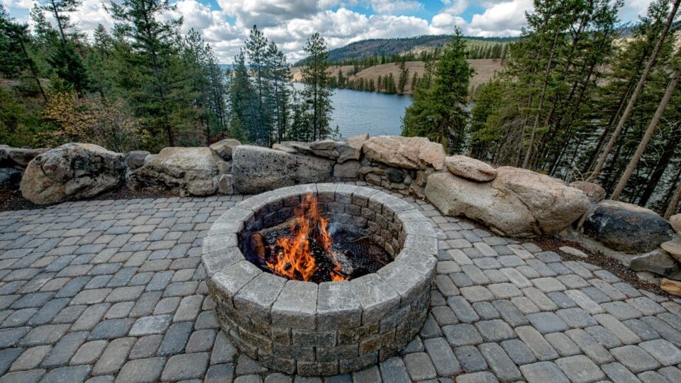 Fire pit sits atop a concrete paver patio above a lake